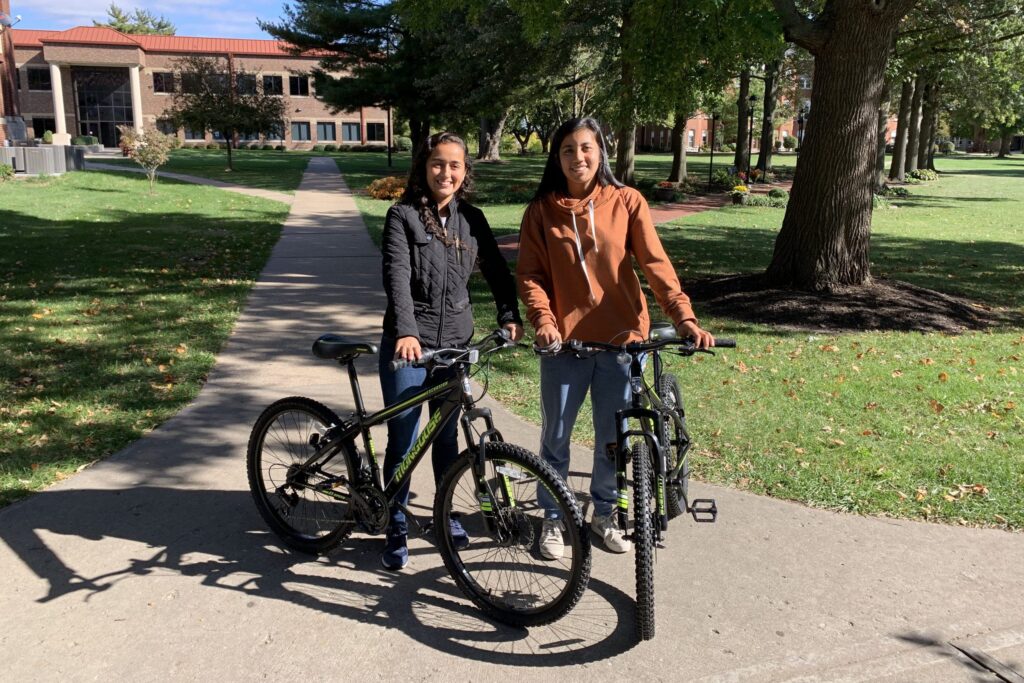 Campus Chaplain Two students standing with bicycles on a campus sidewalk