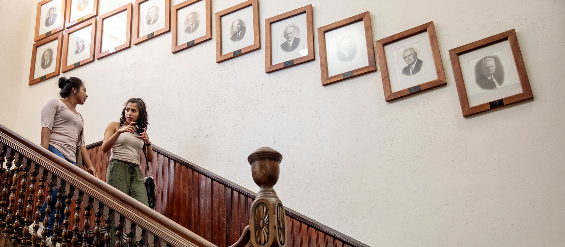 Leadership Two students on a staircase lined with framed portraits
