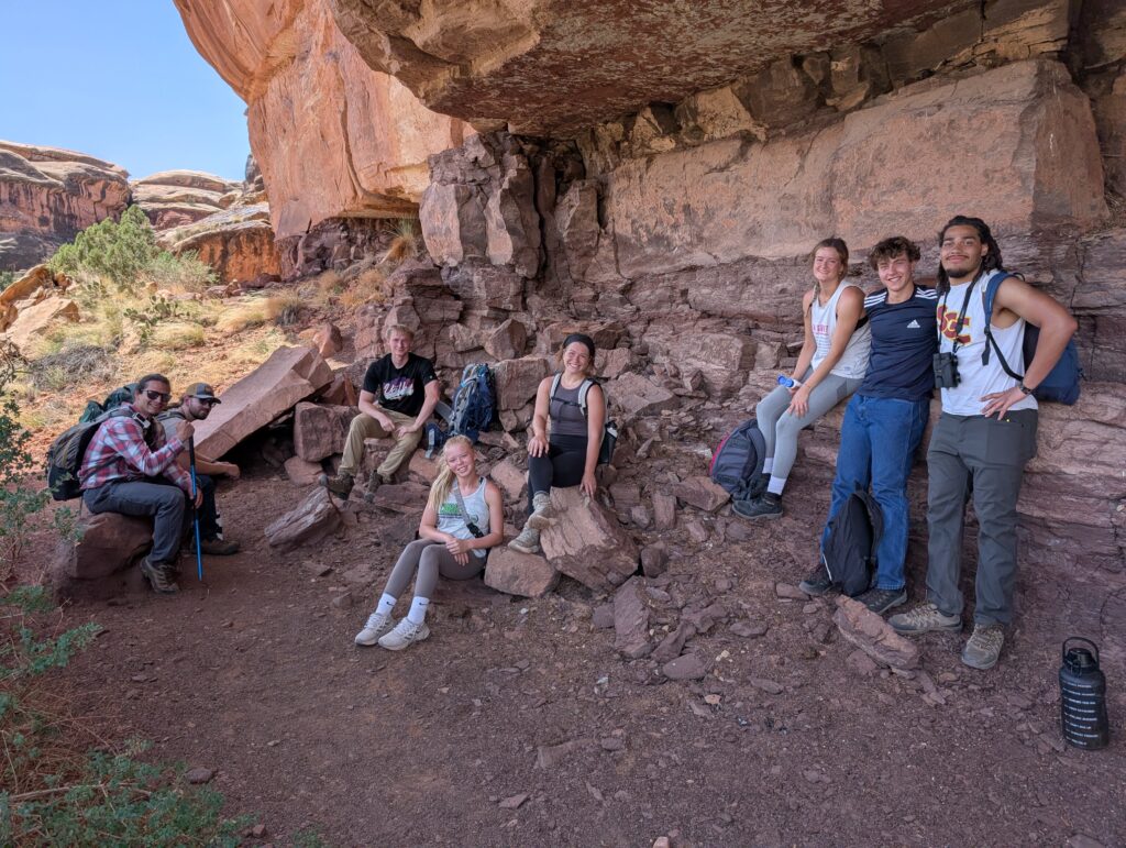 Biology (Bachelor's) A group of students rests beneath a red sandstone overhang during a field biology trip.