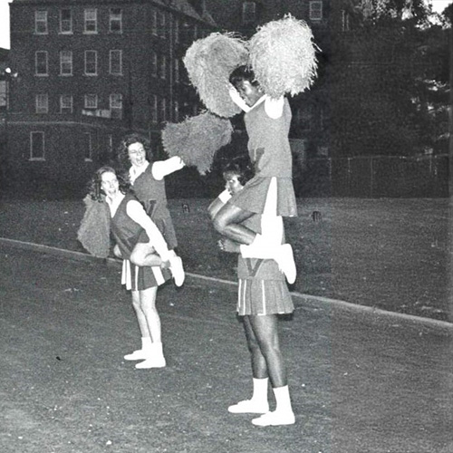 Murrell Library & Academic Support Center Archival photo of cheerleaders with pom-poms performing a stunt on a campus lawn.