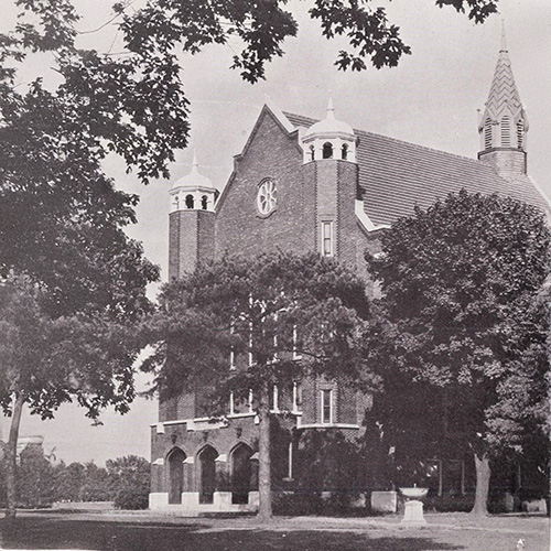 Murrell Library & Academic Support Center Archival photo of a brick campus building with towers and a clock face, framed by trees.
